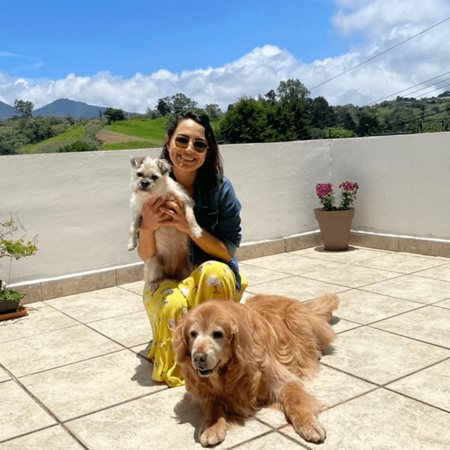 Mujer feliz con lentes oscuros posa con un perrito en brazo y otro a sus pies en una terraza